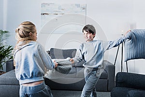 Little siblings in pajamas fighting with pillows at home