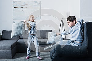 Little siblings in pajamas fighting with pillows at home