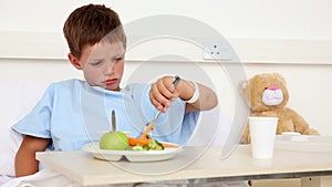 Little sick boy sitting in bed having lunch