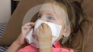 A little sick girl blows her nose and coughs into a paper napkin while lying in bed.