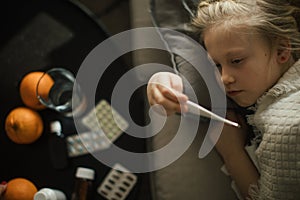 Little sick girl measuring her body temperature.