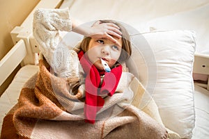 Little sick girl measuring temperature and holding hand on head