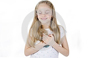 Little sincere adorable girl closed eyes holding hands on chest feeling gratitude pose. Arms on heart gesture of love appreciation