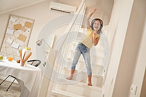 Little singer. Cute and happy caucasian girl wearing headphones standing on stairs and listening music, she is singing