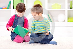 Little sister and brother reading from an interesting book