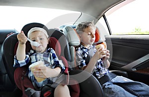 Little sister and her brother in safety car seat eating sweet ice cream. The little girl is capricious