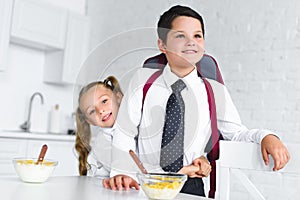 little sister hugging brother in school uniform with backpack at table with breakfast in kitchen at home back to