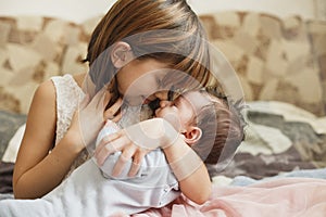 Little sister hugging her newborn brother. Toddler kid meeting new sibling. Cute girl and new born baby boy relax in a