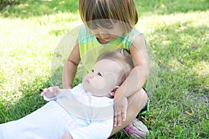 Little sisters in the backyard. Smiling kids sitting on grass in summer. Children in family: toddler and baby portrait