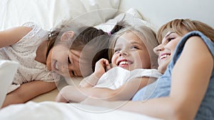 Little sisters embracing and sharing dreams with mother in bed