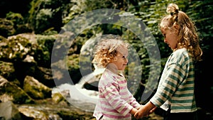 Little sisters hold hands at beautiful Alpine waterfall in the woods