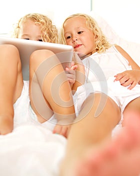 Little sisters lying on bed and using digital tablet