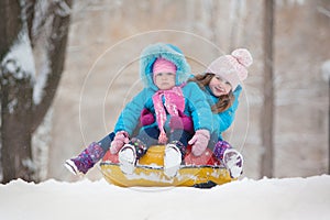 Little sisters ride a snow tube from a hill winter time