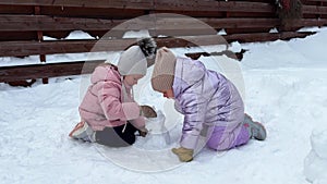 Little sisters twins making a little snowman sitting on the snow