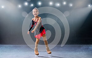 Little skater rides on rings in red and black dress on ice arena