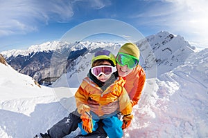 Little skier, father sit in snow on mountain peak