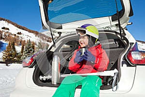 Little skier sitting in car boot and drinking tea