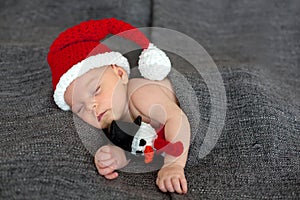 Little sleeping newborn baby boy, wearing Santa hat and holding