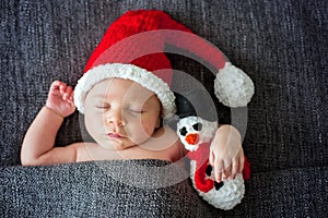 Little sleeping newborn baby boy, wearing Santa hat and holding