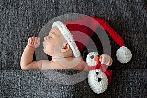 Little sleeping newborn baby boy, wearing Santa hat and holding