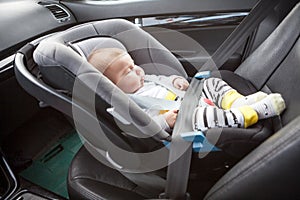 Little sleeping three month old baby child fastened with security belt in safety car seat