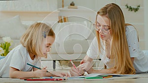 Little small adopted child girl enjoy art draw with Caucasian mother in glasses lying at home floor together. Daughter