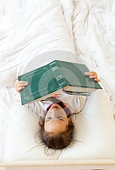 Little smart girl reading big old book in bed