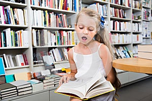 Little smart girl reading a book in the school library