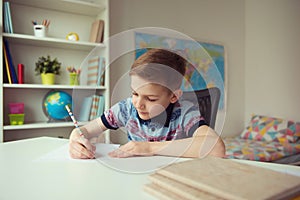 Little smart school boy making homework at desk in room