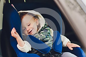 Little smiling baby child fastened with security belt in safety car seat.