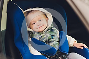 Little smiling baby child fastened with security belt in safety car seat.