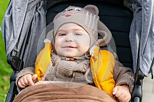 Little smiling baby in stroller. Close up portrait of cute toddler boy covered with a blanket outdoors. Walking with a