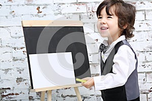 Little smiling boy in bow tie stands next to chalk board