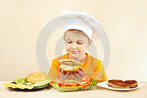 Little smiling boy in chefs hat preparing hamburger