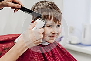 Close-up of woman hands grooming kid boy hair in barber shop.