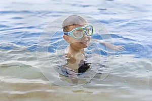Little smiling boy in swimming goggles in the outdoor pool. Copy space