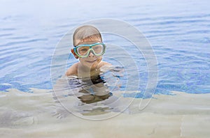 Little smiling boy in swimming goggles in the outdoor pool. Copy space