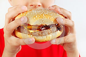 Little smiling boy is tasting the hamburger on white background close up