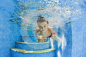 Little smiling child swimming underwater in pool