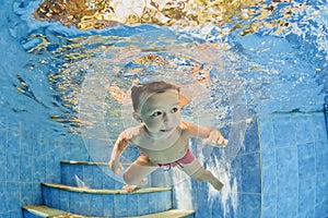 Little smiling child swimming underwater in pool