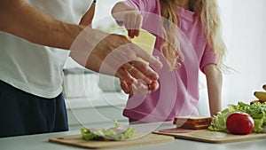 Little smiling daughter stands in the kitchen at the table and helps her father to prepare and fold a sandwich for