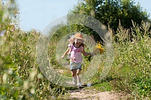 A little smiling girl with a bouquet of field summer flowers running along the path of a forest