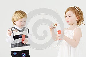 Little smiling girl and boy blow bubbles on white