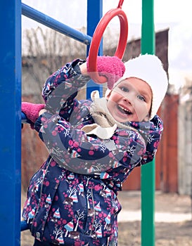 Little smiling girl  in casual autumn or winter clothes on playground climbing rope and athletic rings.  Healthy leisure time with