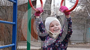 Little smiling girl  in casual autumn or winter clothes on playground climbing rope and athletic rings.  Healthy leisure time with