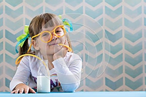 Little smiling girl drinking milk with funny glasses straw