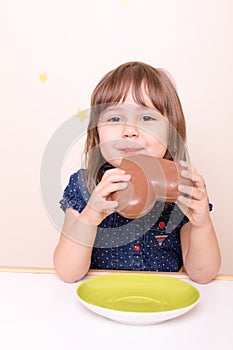 Little smiling girl eating chocolate heart