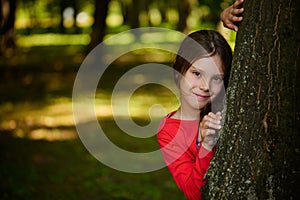 Little smiling girl is hiding behind tree