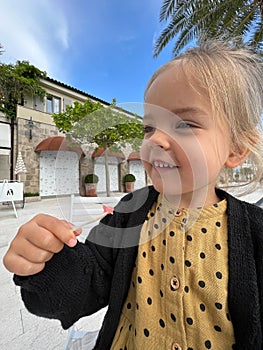 Little smiling girl holding a spatula with a piece of ice cream in her hand