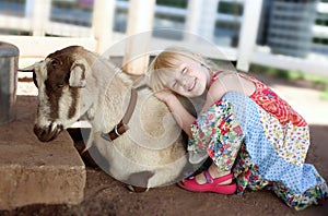 Little smiling girl hugging the goat